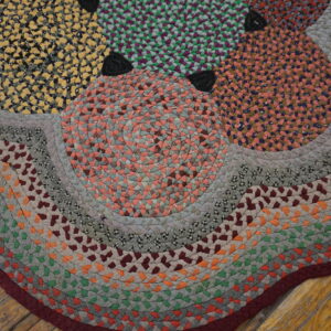 Close-up of a brightly colored braided rug with segmented geometric patterns resting on worn wood flooring.