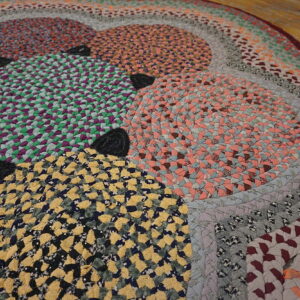Multicolor braided rug featuring circles and concentric rings in yellow, green, and peach on wood flooring.