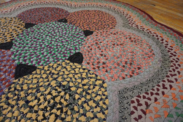 Multicolor braided rug featuring circles and concentric rings in yellow, green, and peach on wood flooring.