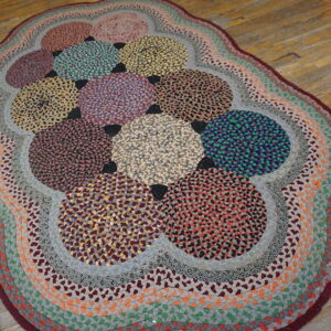 Multicolored oval braided rug with large speckled circles and banded borders resting on light wood flooring.
