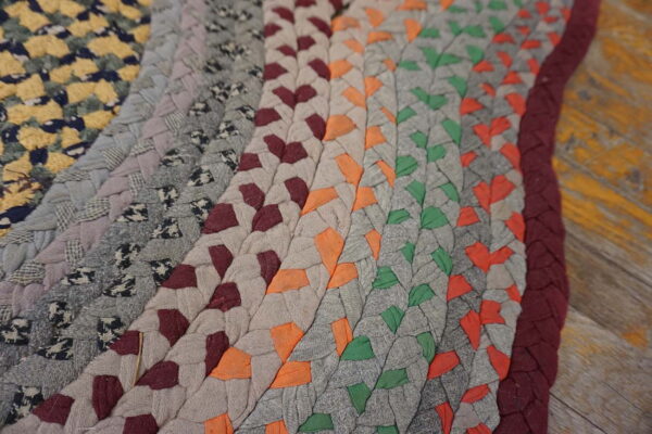 Braided rug detail featuring concentric rows of multicolor fabric patches on distressed gray and yellow wood flooring.