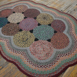 Multicolored braided rug with large circular patterns and a scalloped border on distressed wood planks.