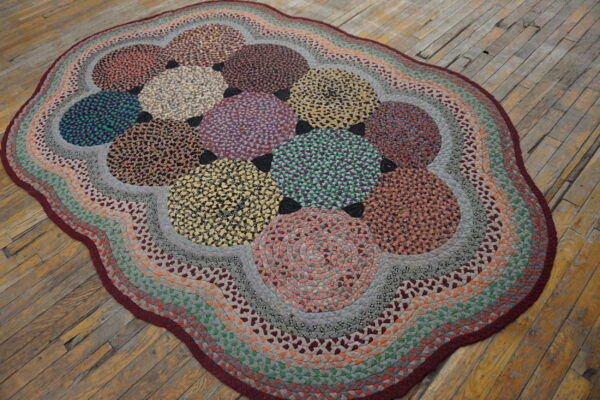 Multicolored braided rug with large circular patterns and a scalloped border on distressed wood planks.