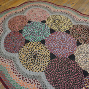A multicolored, braided rag rug featuring overlapping circles rests upon worn wood plank flooring.