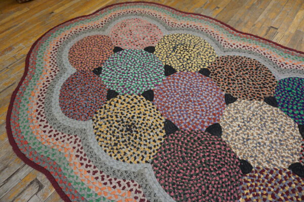 A multicolored, braided rag rug featuring overlapping circles rests upon worn wood plank flooring.