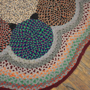 Multicolor braided rug with purple, green, orange, and gray patches on rustic wooden floorboards.
