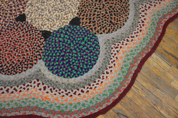 Multicolor braided rug with purple, green, orange, and gray patches on rustic wooden floorboards.