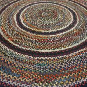 Close-up of a circular braided rug displaying concentric rings of multicolored, variegated fabric strips.