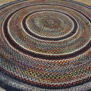 A round, braided, multicolored rug featuring concentric rings rests on light wooden plank flooring.