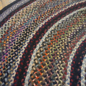 Close-up of a multicolored braided round rug featuring concentric rings on light wooden plank flooring.
