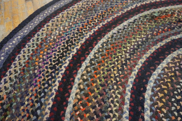 Close-up of a multicolored braided round rug featuring concentric rings on light wooden plank flooring.