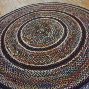 Multicolor braided round rug with dark concentric rings rests on distressed light wood plank flooring.