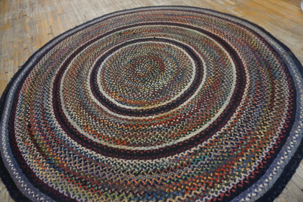 Multicolor braided round rug with dark concentric rings rests on distressed light wood plank flooring.