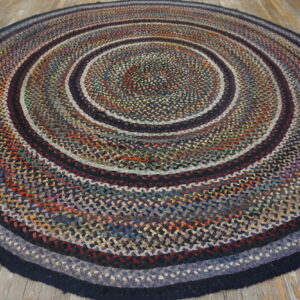 Circular braided rug in variegated blue, red, and black concentric rings on light wood flooring.