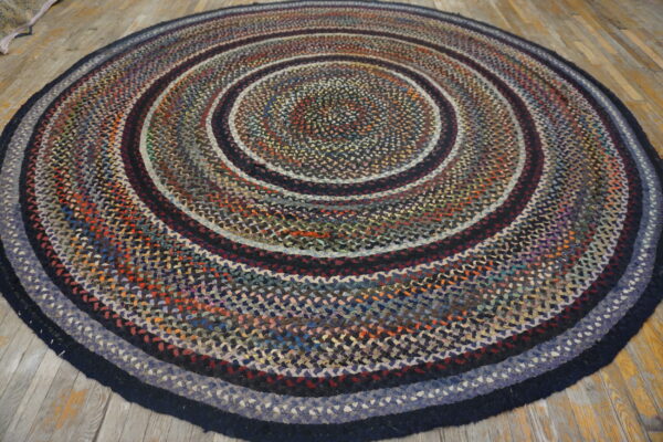 Circular braided rug in variegated blue, red, and black concentric rings on light wood flooring.