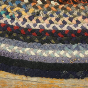 Thick multicolored braided rug featuring concentric bands of blue, black, red, and neutral tones on wood flooring.