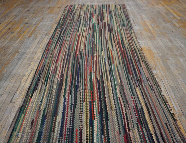 Multicolor, textured runner rug with vertical strips of various colors laid on gray and yellow wooden planks.