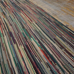 A multicolored braided rag rug with diagonal stripes covers rustic wood flooring.