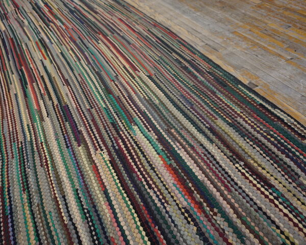 A multicolored braided rag rug with diagonal stripes covers rustic wood flooring.