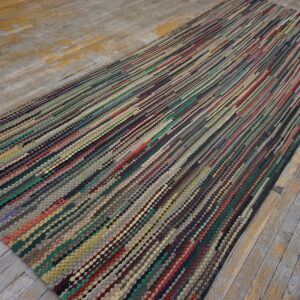 A long, textured runner rug featuring dense, vertical multicolored stripes rests on weathered gray wood flooring.