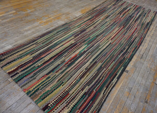 A long, textured runner rug featuring dense, vertical multicolored stripes rests on weathered gray wood flooring.