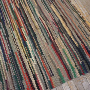 A multicolored braided rag rug with chunky vertical stripes lies on distressed, light wood flooring.
