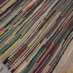 Textured, multi-colored rug with diagonal braided lines rests on distressed wood plank flooring.
