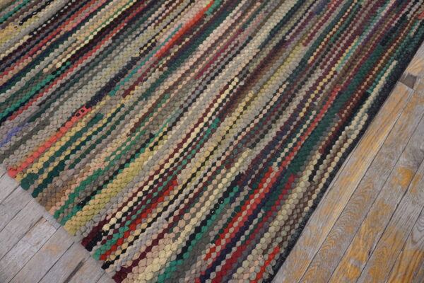 Textured, multi-colored rug with diagonal braided lines rests on distressed wood plank flooring.