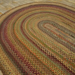 A multi-colored braided oval rug in earthy browns, greens, and maroon rests on worn wooden planks.