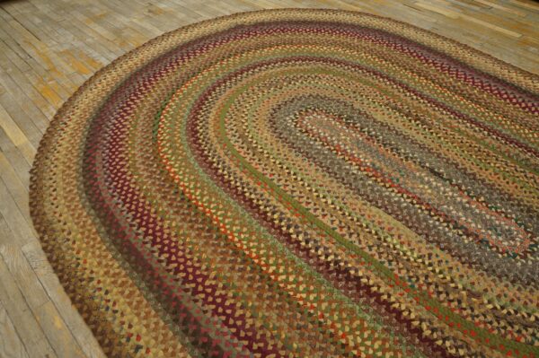 A multi-colored braided oval rug in earthy browns, greens, and maroon rests on worn wooden planks.