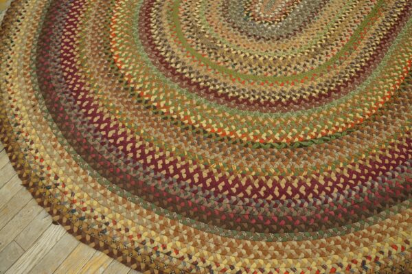A round braided rug in concentric rings of brown, green, and maroon rests on light wood flooring.