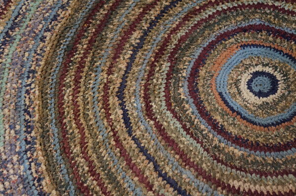 Close-up of a chunky braided rug forming concentric circles in diverse earth tones, blues, and maroon.