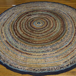 Round textured rag rug featuring concentric circles of blue, beige, and maroon on a hardwood floor.
