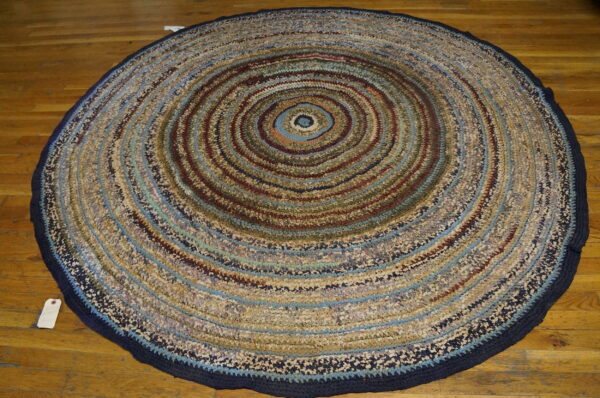 Round textured rag rug featuring concentric circles of blue, beige, and maroon on a hardwood floor.