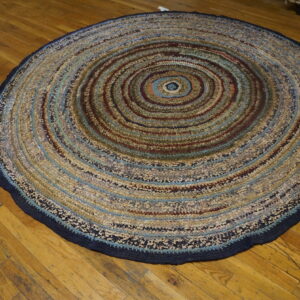 A round, multicolored braided rug with concentric stripes rests on rustic wooden flooring.
