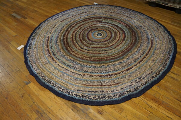A round, multicolored braided rug with concentric stripes rests on rustic wooden flooring.