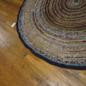 Braided round rug with concentric circles of brown, tan, and blue rests on distressed wood flooring.