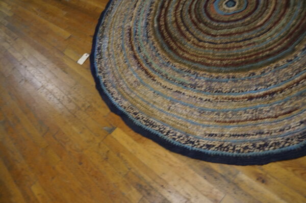 Braided round rug with concentric circles of brown, tan, and blue rests on distressed wood flooring.