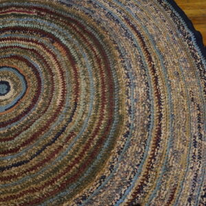 Round coiled rug featuring variegated blue, brown, red, and beige colors on wood plank flooring.