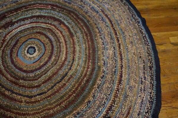 Round coiled rug featuring variegated blue, brown, red, and beige colors on wood plank flooring.
