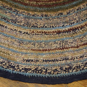 Close-up of a textured round rug featuring variegated concentric stripes of blue, tan, and maroon on a wooden floor.