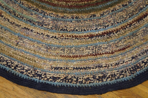 Close-up of a textured round rug featuring variegated concentric stripes of blue, tan, and maroon on a wooden floor.