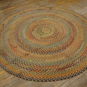 Round, chunky multicolored braided rug in earthy tones rests on worn hardwood plank flooring.