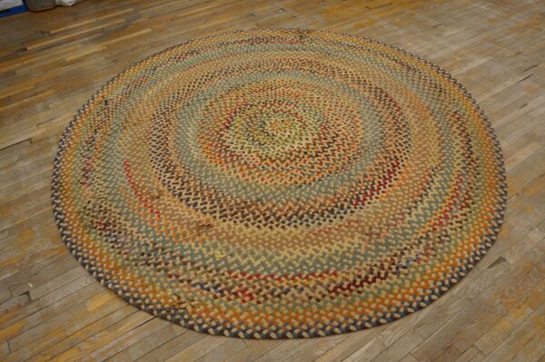 Round, chunky multicolored braided rug in earthy tones rests on worn hardwood plank flooring.