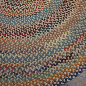 Close-up of a round braided rug featuring variegated bands of blue, rust, and earth-toned patches on wood flooring.