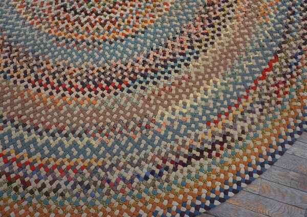 Close-up of a round braided rug featuring variegated bands of blue, rust, and earth-toned patches on wood flooring.