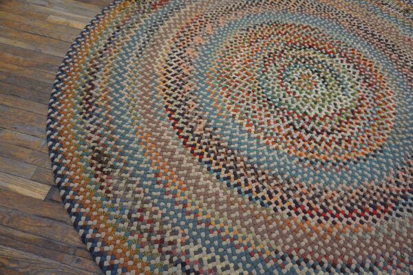 Circular braided rug featuring a multicolored patchwork design rests upon warm brown wood planks.