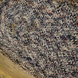 Heavily textured woven rug with multicolored blocks of white, blue, red, and black on wood planks.