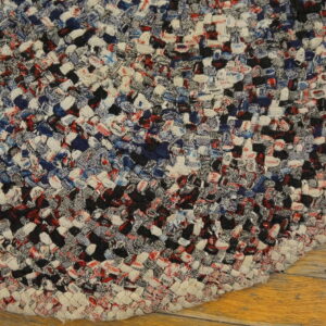 Braided multicolored rug in red, navy, black, and white resting on light wood flooring.
