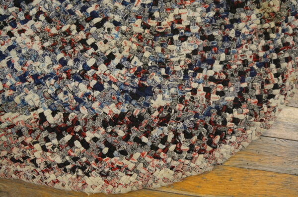 Braided multicolored rug in red, navy, black, and white resting on light wood flooring.